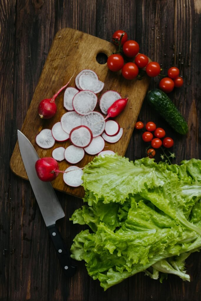 Top-down view of fresh radishes, cherry tomatoes, and lettuce on a cutting board.